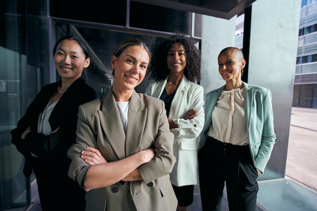 team portrait diverse female professionals confident posing outside business center. group happy.